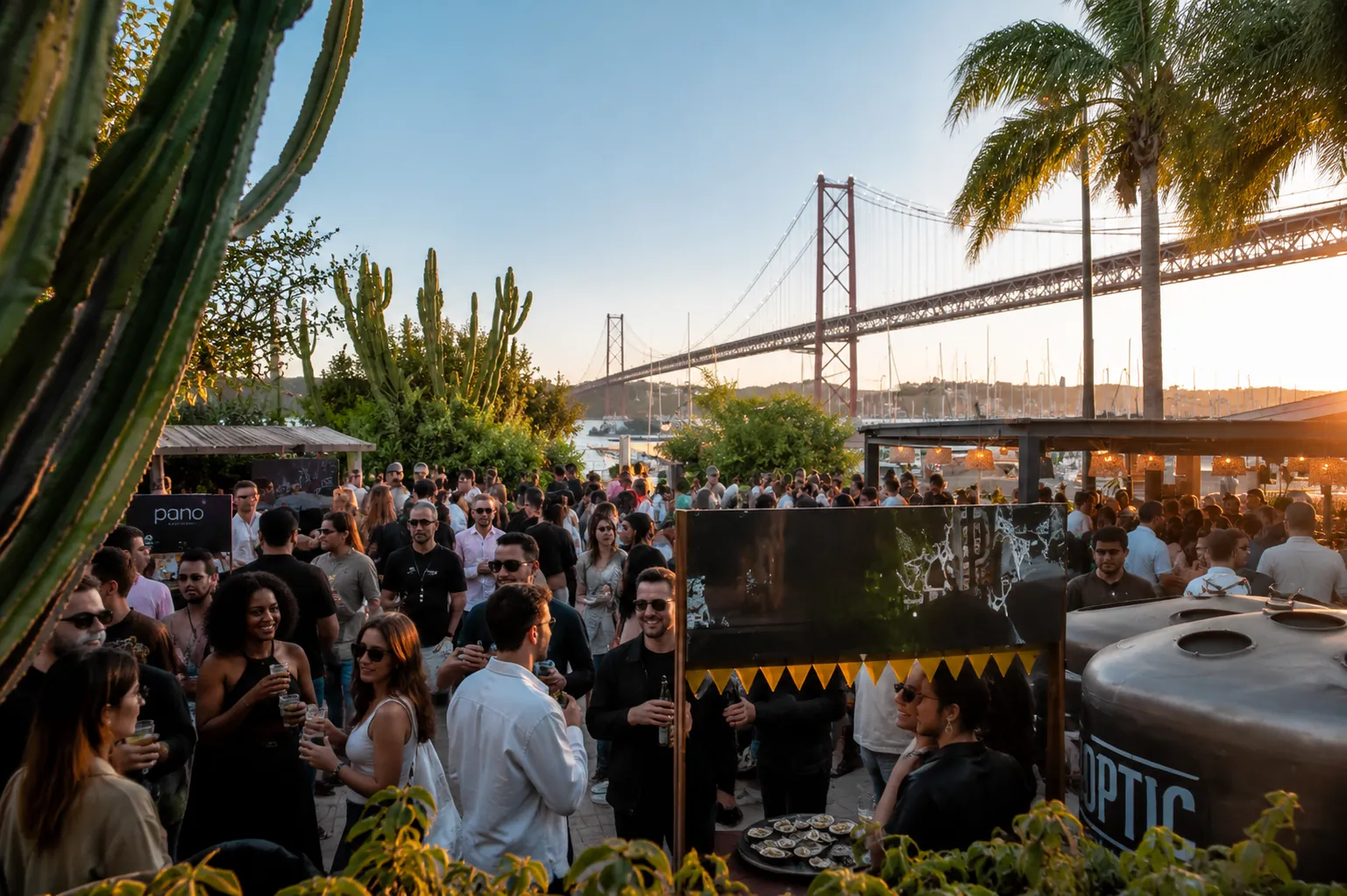 Guests at a CH3-produced riverside reception in Lisbon at sunset, with the 25 de Abril bridge behind