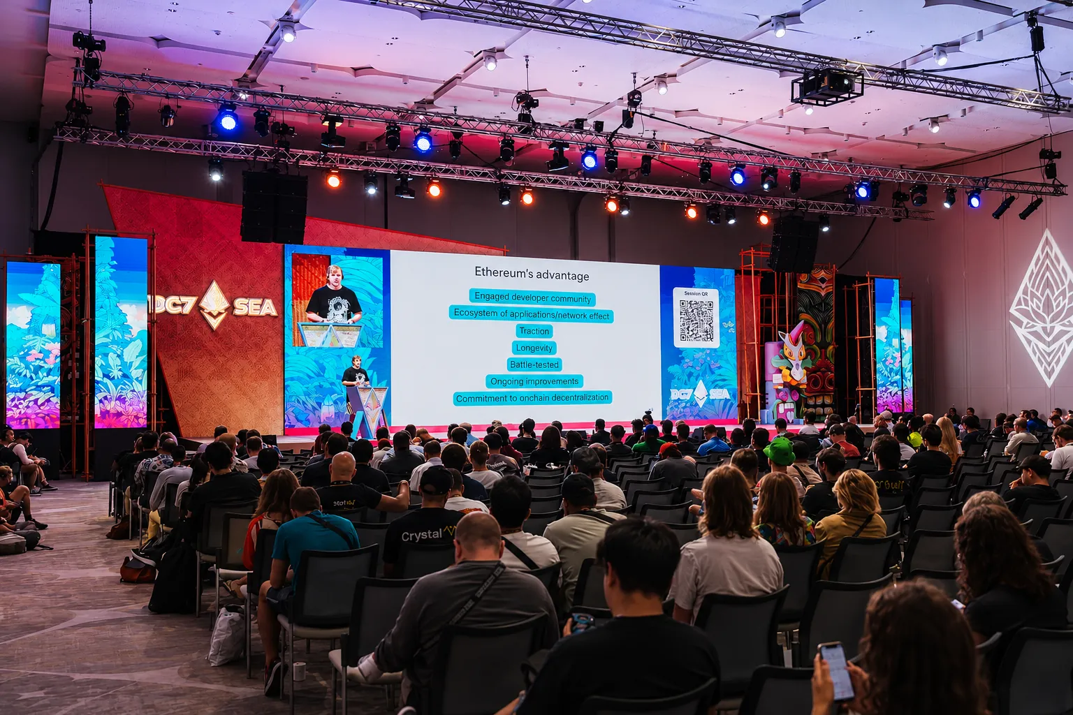 Attendees seated in a full auditorium facing the Devcon main stage, with a speaker presenting on a large screen