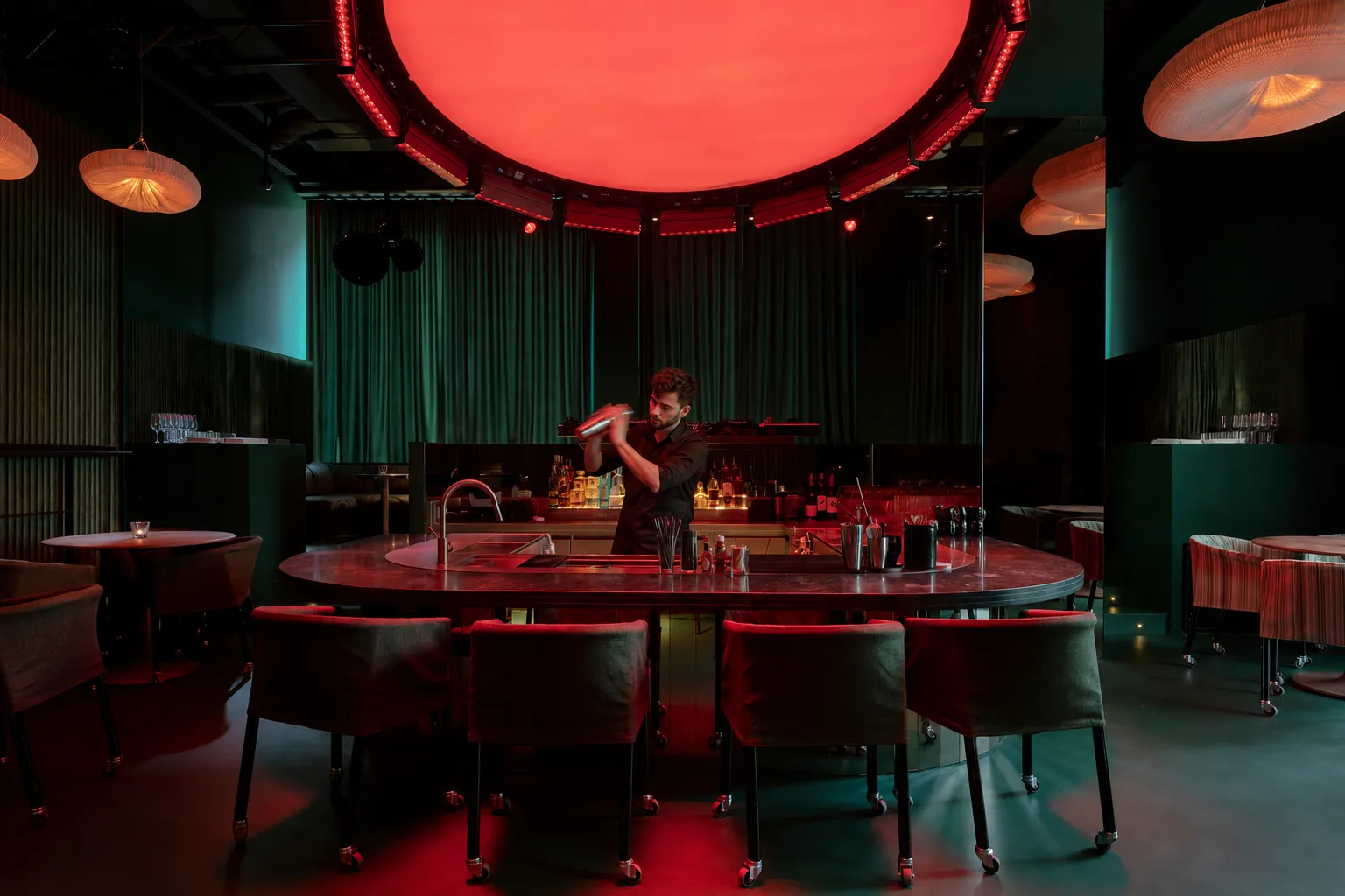 Bartender mixing cocktails in a moody red-lit cocktail bar in Barcelona, Spain