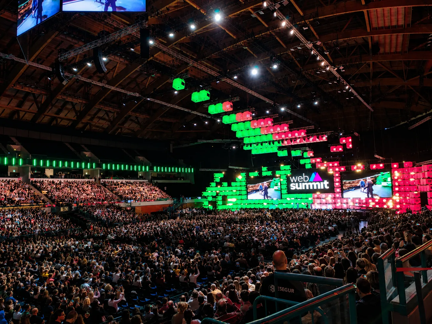 Packed Altice Arena during Web Summit in Lisbon, crowd filling the floor and tiers in front of the green and red LED stage