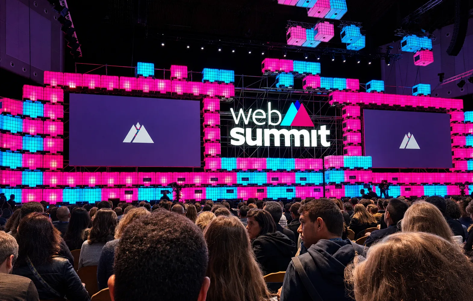 Web Summit main stage in Lisbon lit in pink and blue LED cubes, with a full seated audience facing the screens