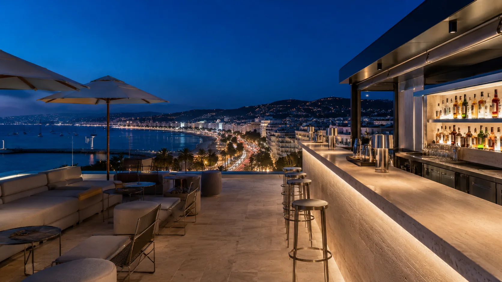 A rooftop bar terrace at dusk overlooking the Cannes Croisette and the bay