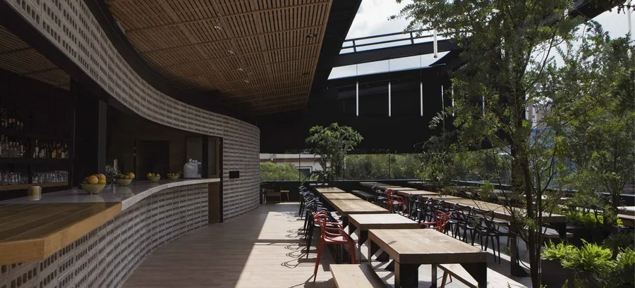 Long communal timber tables and a curved brick bar on the covered roof terrace at Balmori Roofbar, Roma Norte, Mexico City