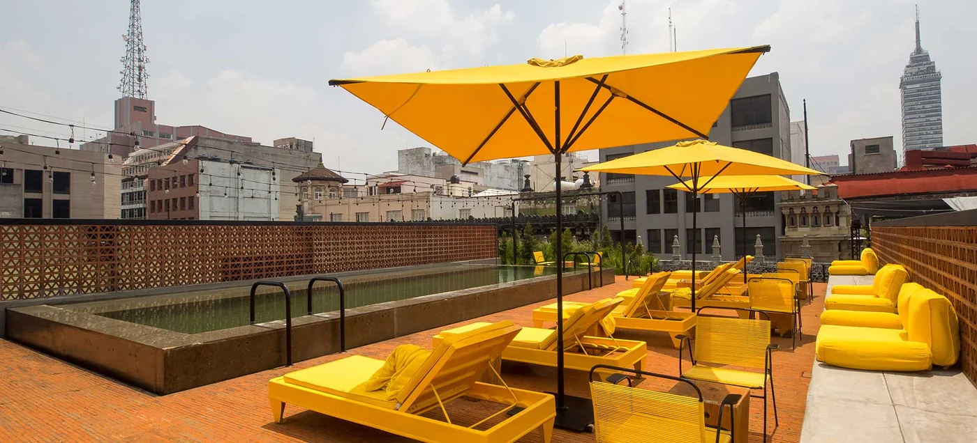 Rooftop pool terrace with yellow parasols and the Torre Latinoamericana behind at Downtown México, Centro Histórico