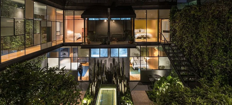 Lit glazed rooms around a planted courtyard at night at Ignacia Guest House, Roma Norte, Mexico City