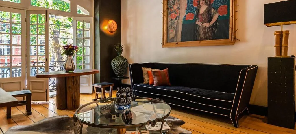 Sitting room with a dark velvet sofa, glass coffee table and tall balcony doors at La Valise, Roma Norte, Mexico City