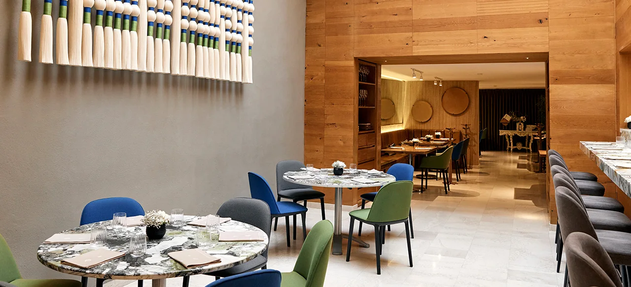 Dining room with marble tables, coloured chairs and a wood-panelled wall at Quintonil, Polanco, Mexico City