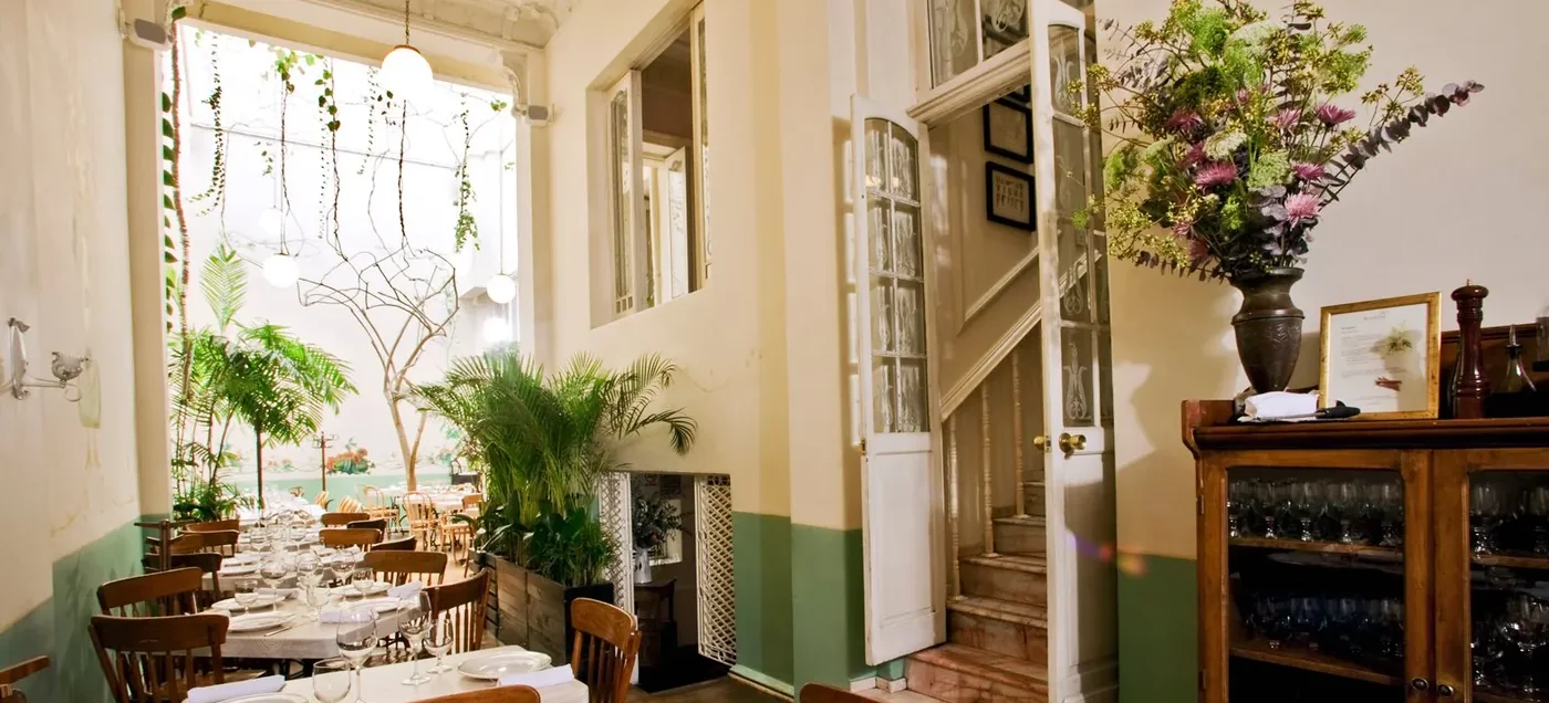 Dining room of a converted Roma Norte townhouse with a marble staircase, tall windows and hanging plants at Rosetta, Mexico City